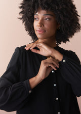 Woman wearing a black blouse with button details against a beige background
