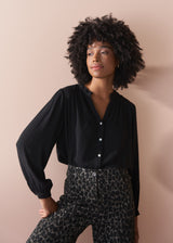 Woman wearing a black blouse and leopard print trousers against a beige background