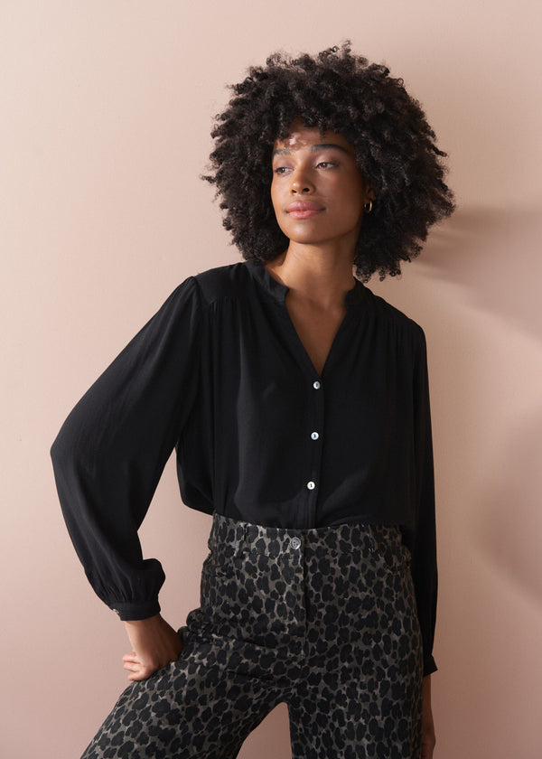 Woman wearing a black blouse and leopard print trousers against a beige background