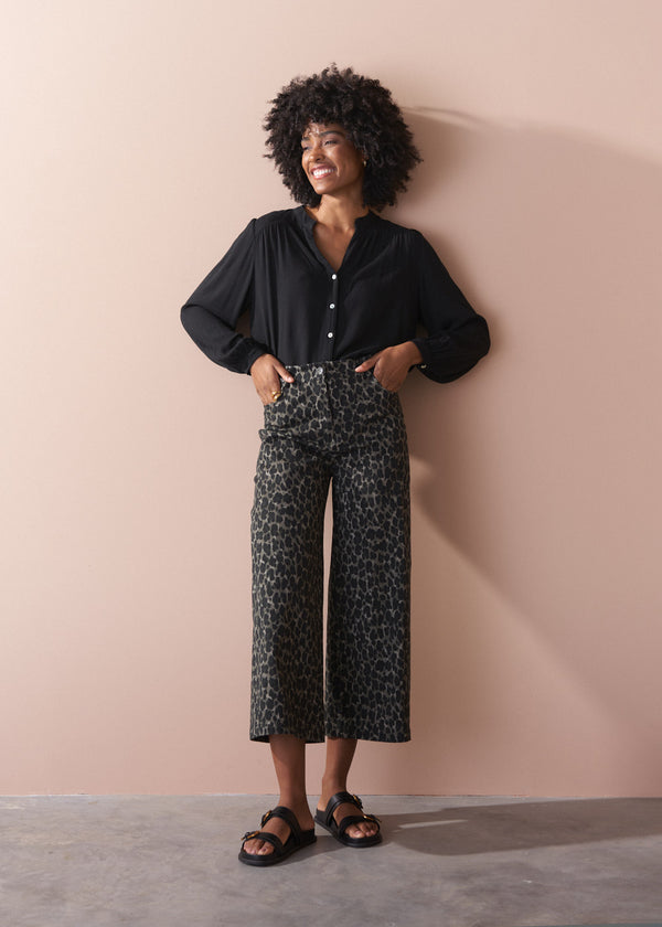 Woman wearing a black shirt and leopard print trousers against a beige wall