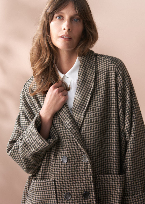 Woman wearing a houndstooth patterned coat against a pink background