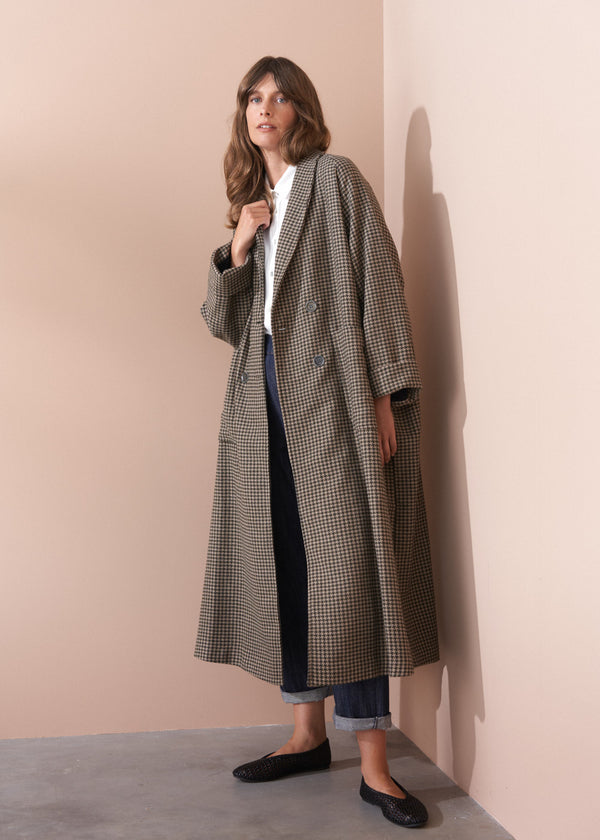 Woman wearing a long checkered coat against a beige wall.