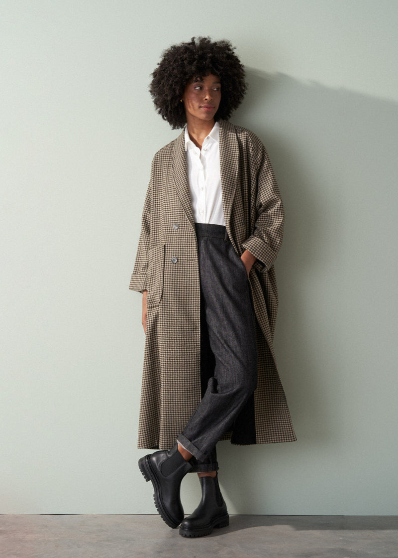 Person wearing an oversized khaki and brown check coat against a plain background