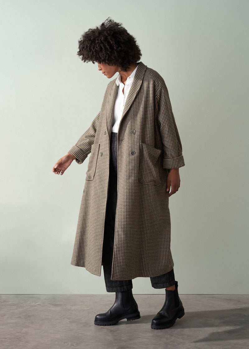 Person wearing a long checkered coat against a plain background