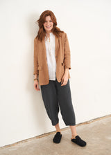 A model wearing a camel coloured linen blazer jacket over a white top with matching camel trousers