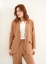 A model wearing a camel coloured linen blazer jacket over a white top with matching camel trousers