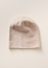 A soft knit beanie hat in a pale blush pink color, displayed flat against a matching light beige background.