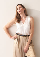 Woman wearing a white sleeveless top against a plain background