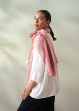 Woman wearing a pink knitted shawl over a white shirt against a plain background