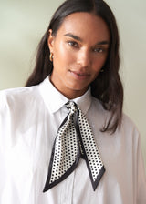 Woman wearing a white shirt with a black and white polka dot scarf around her neck against a plain background
