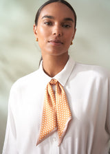 Woman wearing a white shirt with an orange polka dot scarf around her neck against a light background