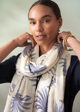 Woman wearing a white scarf with blue patterns, posing against a neutral background