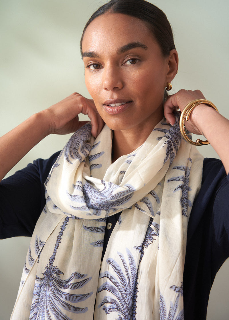 Woman wearing a white scarf with blue patterns, posing against a neutral background