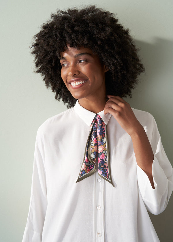 Woman wearing a floral scarf around her neck against a plain background