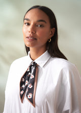 Woman wearing a white shirt with a floral scarf around her neck against a plain background