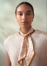 Woman wearing a patterned scarf around her neck against a neutral background