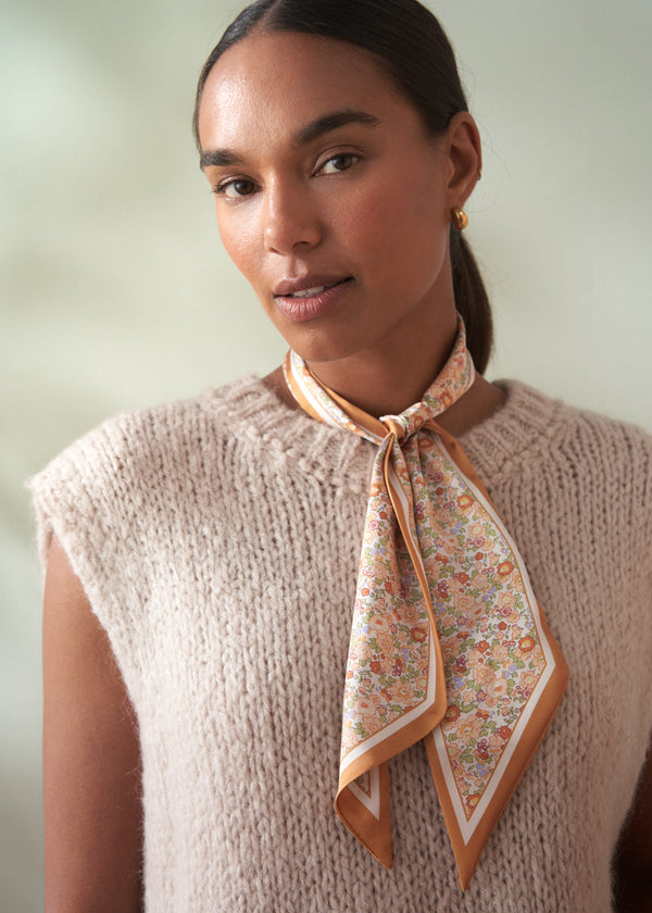 Woman wearing a floral scarf around her neck with a neutral background