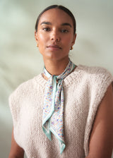 Woman wearing a patterned scarf and beige sleeveless sweater against a plain background