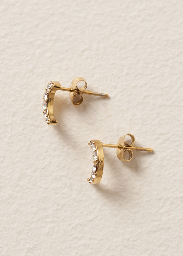 Gold moon stud earrings with embedded crystals on a beige textured background