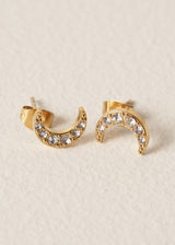 Gold moon stud earrings with embedded crystals on a beige textured background