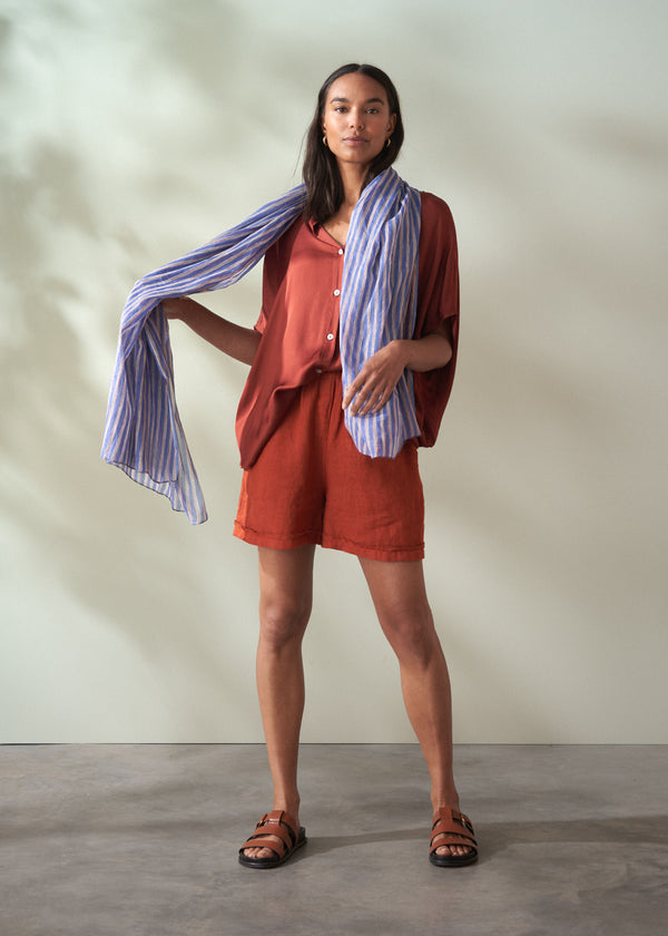 Woman wearing a rust-colored outfit with a striped scarf against a neutral background