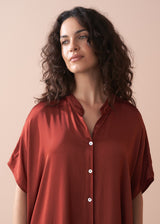Woman wearing a rust-colored shirt against a beige background