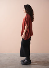 Woman wearing a rust-colored blouse and black pants against a beige background