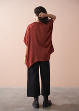 Person wearing a rust-colored oversized top and black pants against a beige background