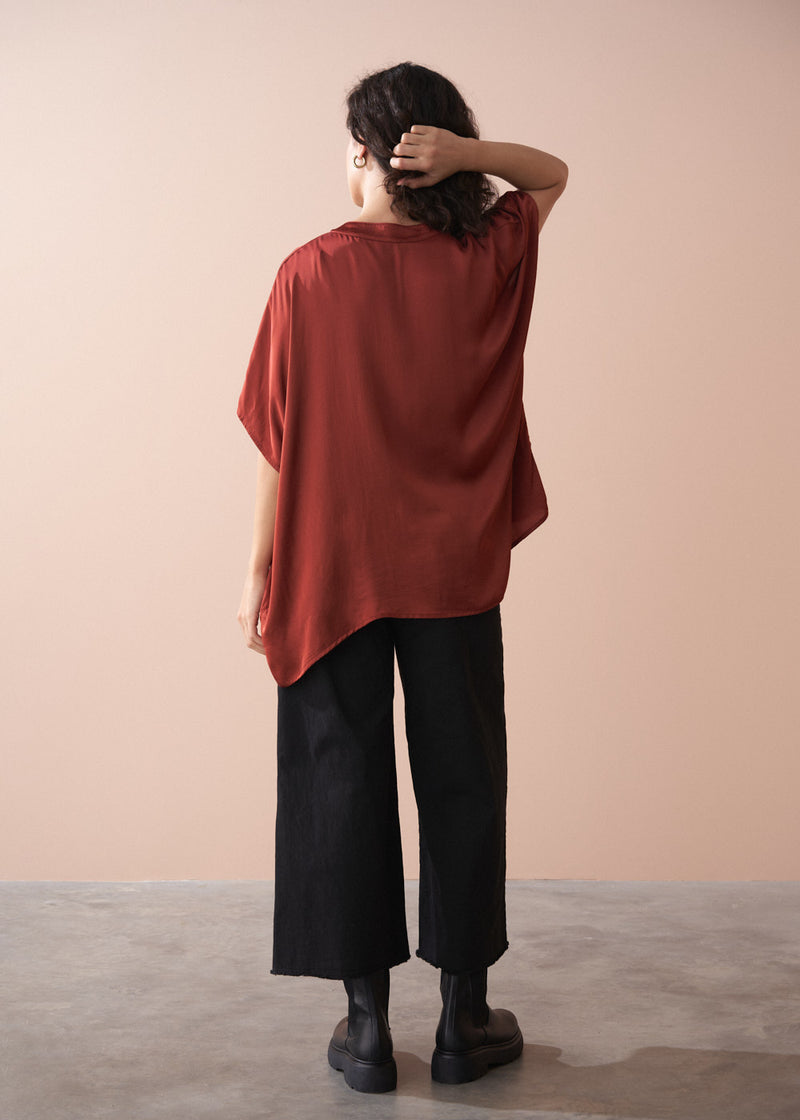 Person wearing a rust-colored oversized top and black pants against a beige background