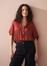 Woman wearing a rust-colored blouse against a beige wall