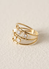 A gold-plated multi-band ring featuring five bezel-set clear round gemstones, photographed on a textured off-white background.