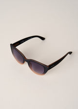 Cat-eye sunglasses with dark lenses and brown frame on a light beige background