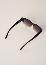 Cat-eye sunglasses with black frame and gradient lenses on a light beige background