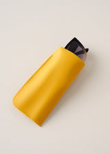 Yellow sunglasses case with a black pair of cat-eye sunglasses inside on a light beige background
