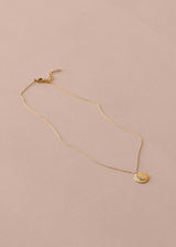 Gold necklace with a round pendant on a beige background