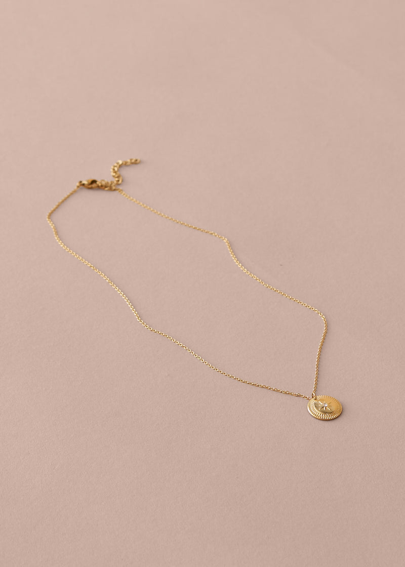 Gold necklace with a round pendant on a beige background