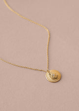 Gold necklace with a round pendant on a beige background