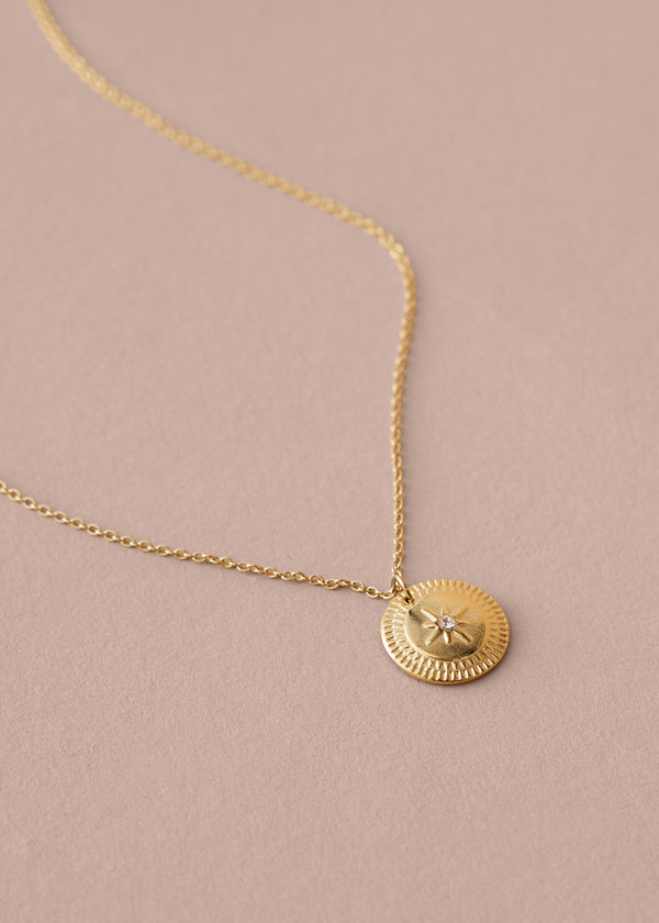 Gold necklace with a round pendant on a beige background