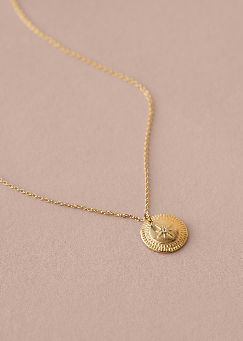 Gold necklace with a round pendant on a beige background