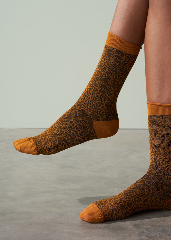 Patterned socks with orange accents worn by a person on a neutral background