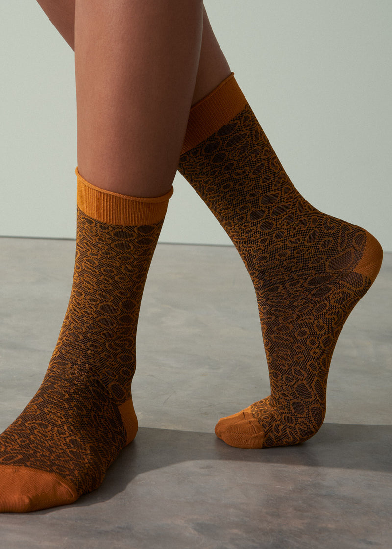 Brown patterned socks with orange accents worn by a person on a neutral background