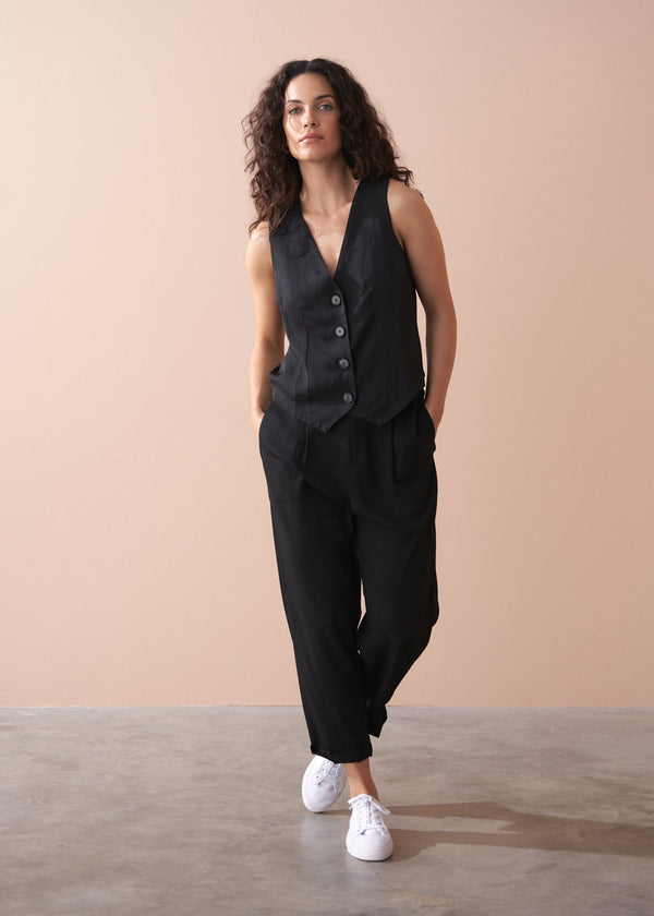 Woman wearing a black button up waistcoat against a beige background