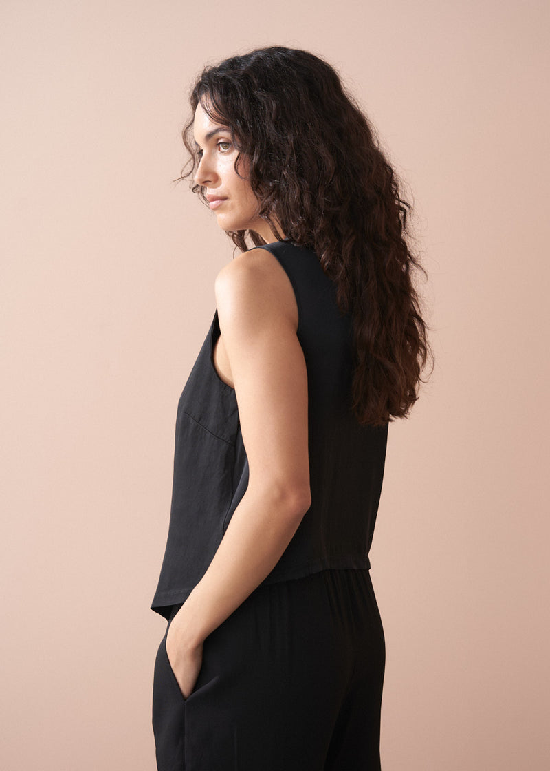 Woman wearing a black button up waistcoat against a beige background