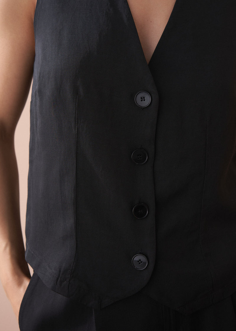 Woman wearing a black button up waistcoat against a beige background