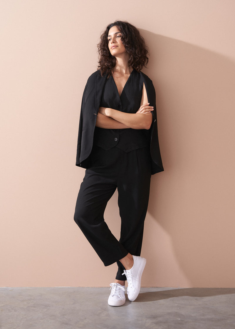 Woman in a black outfit standing against a beige wall