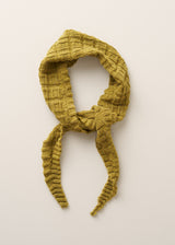A textured mustard yellow knit scarf with a waffle pattern, styled in a loop and tied at the front, set against a plain off-white background.