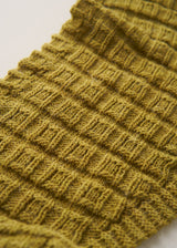 A close-up of a ribbed knit fabric in a muted olive yellow color, showing the detailed texture of the yarn and stitching.