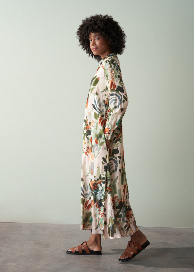 Woman wearing a v-neck floral midi dress with sandals, standing side on against a plain background