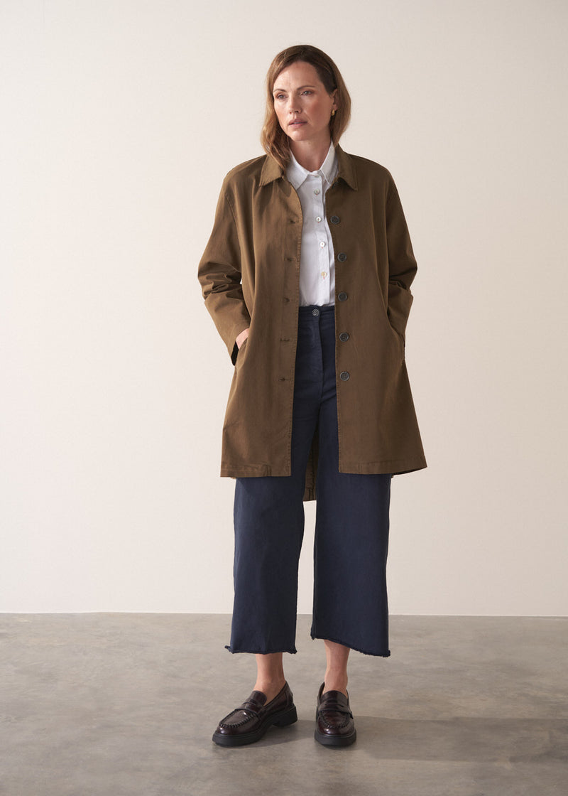 Woman wearing a khaki brown short trench coat over a white shirt on a plain background