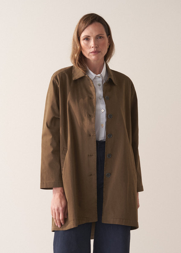 Woman wearing a khaki brown short trench coat over a white shirt on a plain background